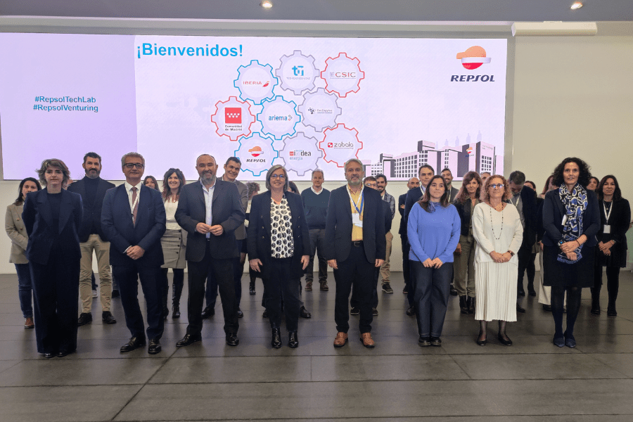 Foto de grupo que muestra a los representantes de las empresas mencionadas de pie. En el fondo de la imagen sale proyectada una diapositiva con los logos de las empresas participantes en el proyecto Madrid Vuela Sostenible